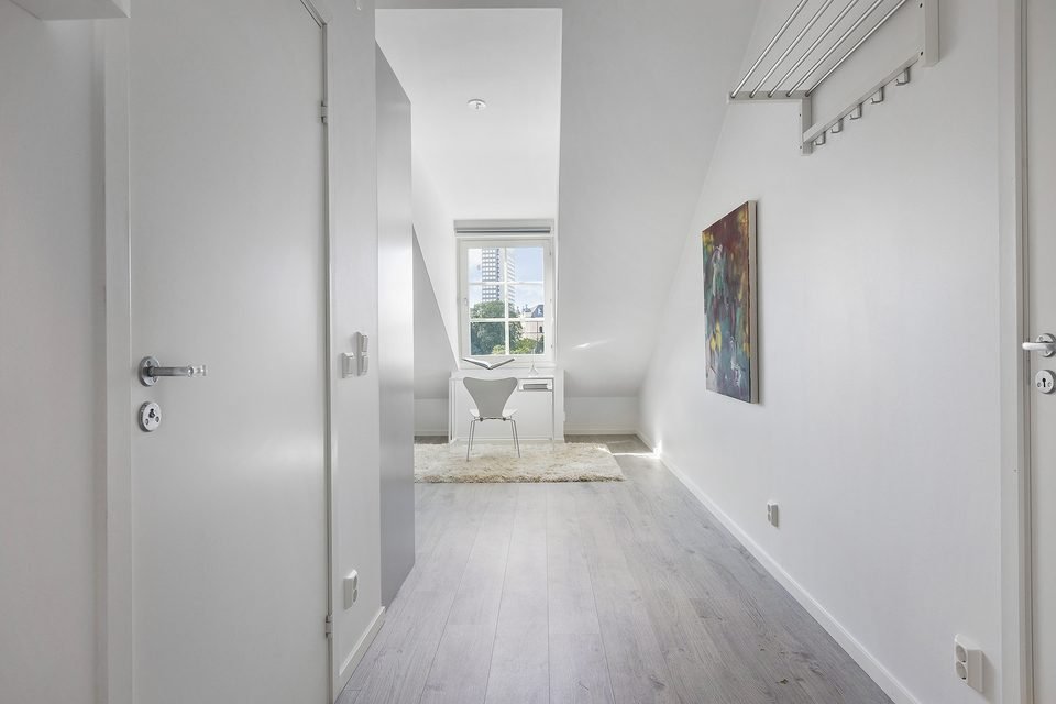 Hall i en lägenhet med vita dörrar, hatthylla och en tavla längre in.