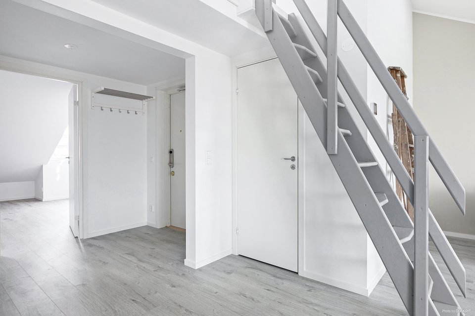 Hall med vita dörrar och trappa i metall upp till entresolplanet.