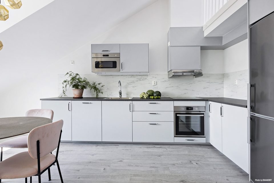 Köksvägg med vita skåpluckor, inbyggd ugn, mikrovågsugn och kylskåp.