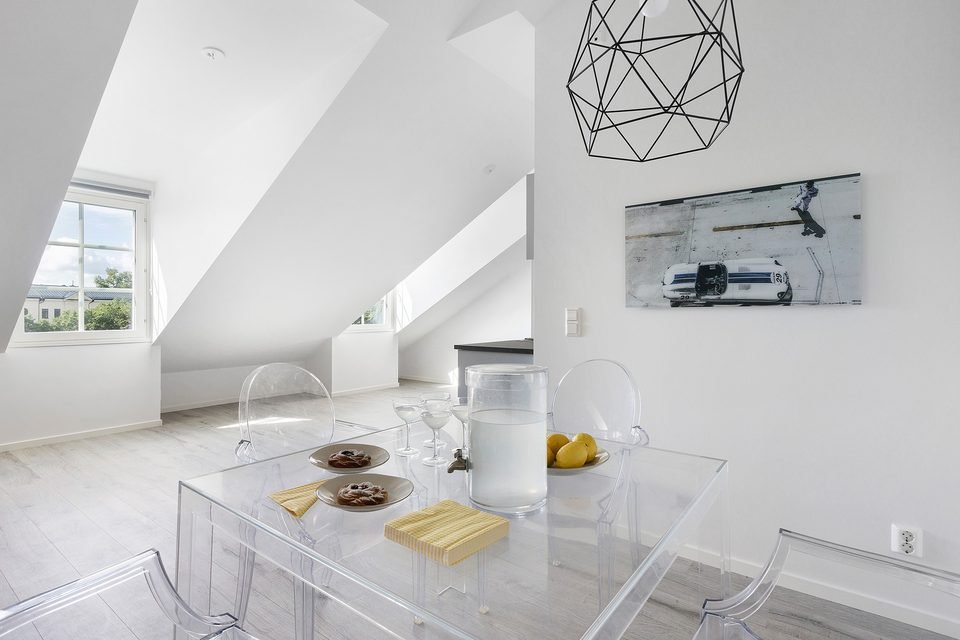 Matbord i glas med stolar under snedtak, med en geometrisk taklampa ovanför.