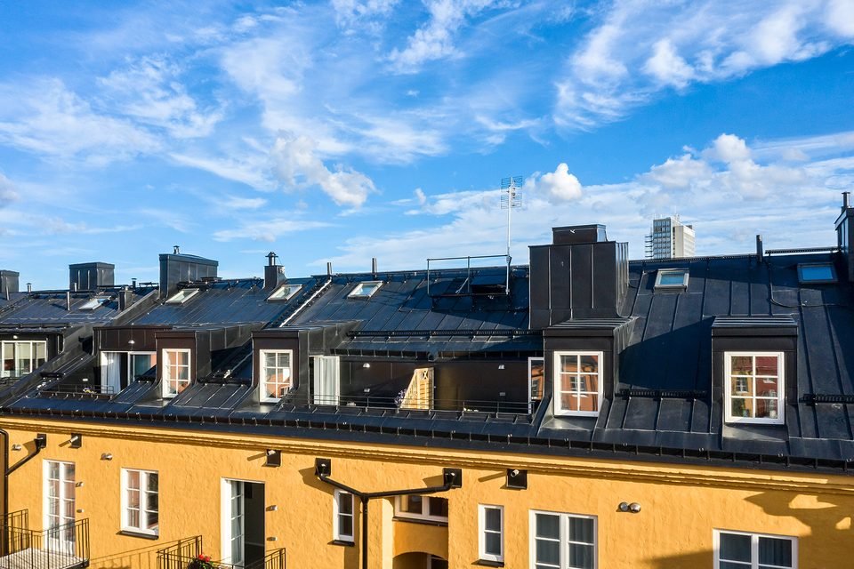 Takåsen med skorstenar och takkupor, med den gula fasaden och balkonger nedanför.