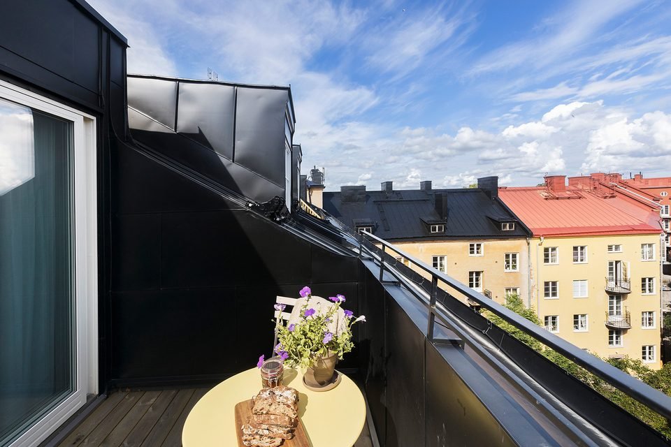 Runt bord med blommor på en takterrass, med hustak och en gul fasad i bakgrunden.