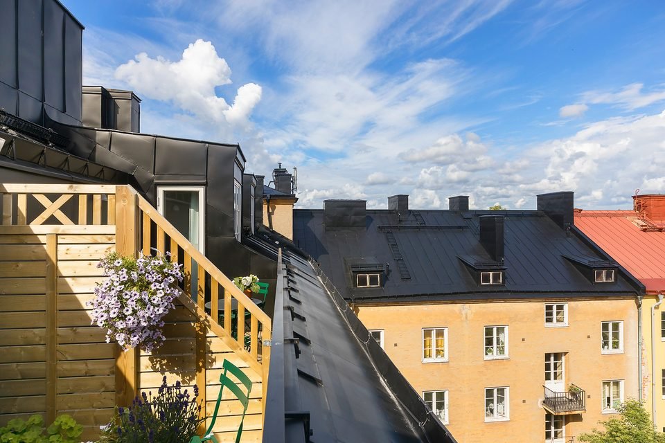 Takterrass med trätrappa, blomlådor och utsikt över gula och röda hustak.