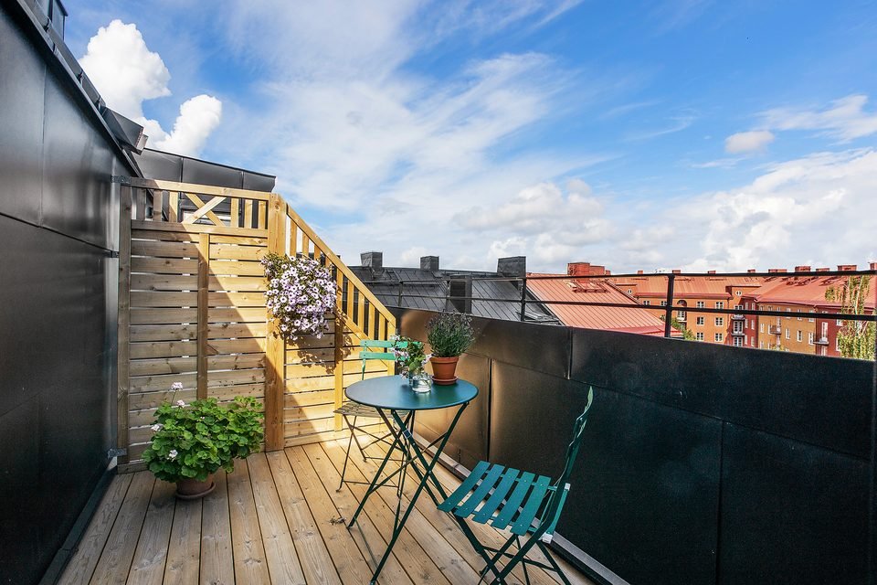 Trädäck på takterrassen med runt bord, stolar och krukväxter.
