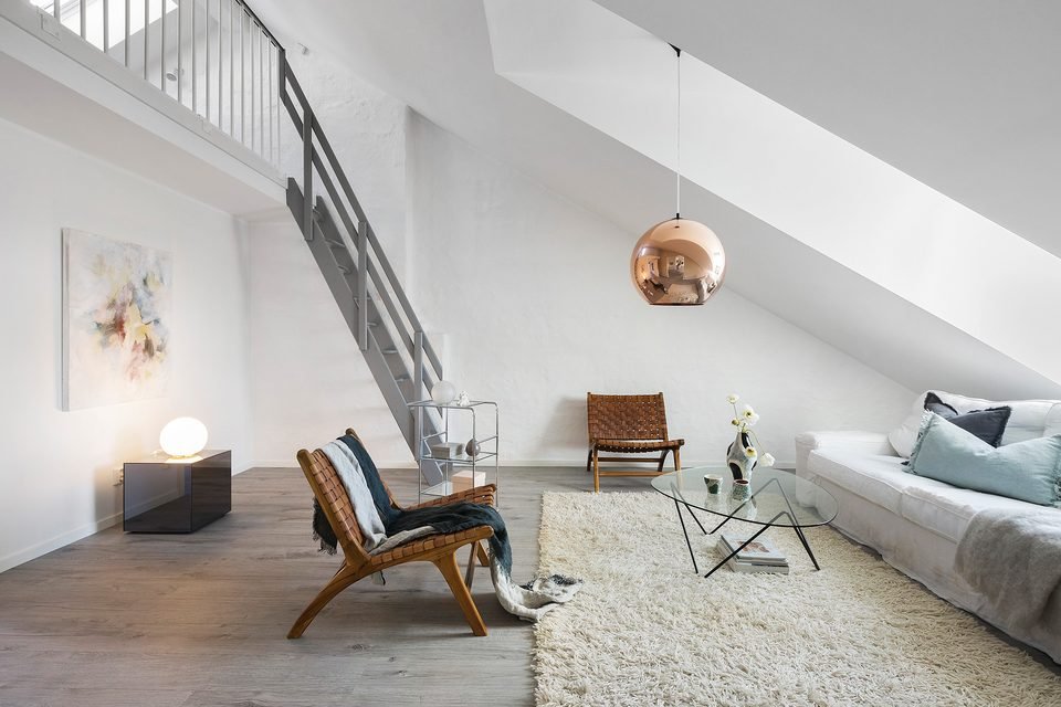 Vardagsrum med soffa, fåtöljer och kopparfärgad taklampa, med trappa upp till entresolplanet.