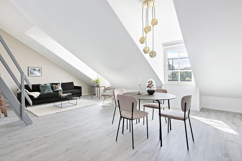 Vardagsrum med soffa och matplats under snedtak, med entresolplan ovanför.