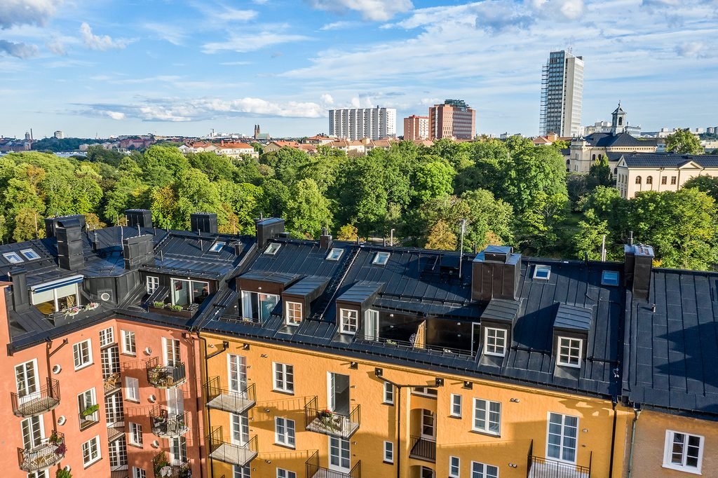 Husets tak och takterrasser sedda ovanifrån, med grönska och Stockholms stadssiluett i bakgrunden.
